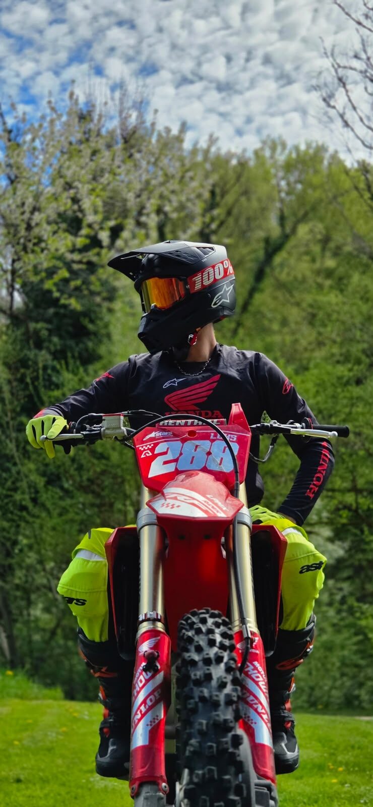Luks sur sa Honda CRF numéro 288, casque, maillot Honda et gants jaunes, devant les arbres.